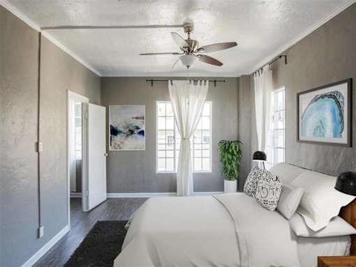 A bedroom with a bed, a ceiling fan, and a painting on the wall.