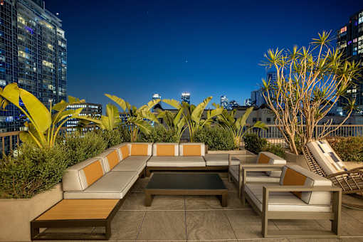 A rooftop patio with a couch, chairs, and plants.