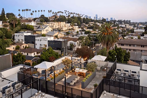 A rooftop patio with a table and chairs overlooks a cityscape.
