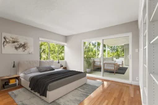 A bedroom with a large bed and a view of a balcony with a couch and plants.