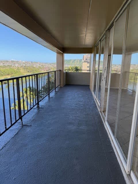 A balcony with a metal railing and glass doors overlooking a hilly landscape.