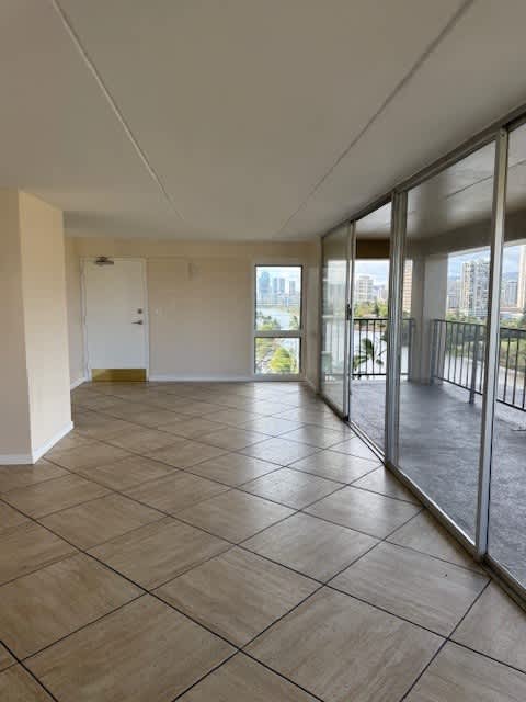 A spacious room with tiled flooring and sliding glass doors leading to a balcony.