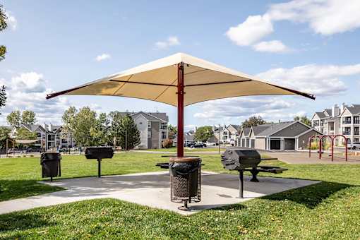 A park with a bench and a trash can under a canopy.