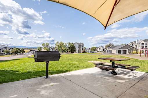 A black mailbox sits on a sidewalk next to a picnic table under a yellow canopy.