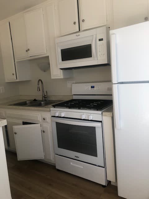 A white kitchen with a stove, oven, microwave, and refrigerator.