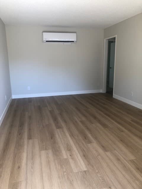 A room with a light brown wooden floor and a white wall with a window.