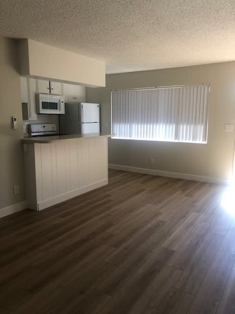 A kitchen with wood flooring and a window with blinds.