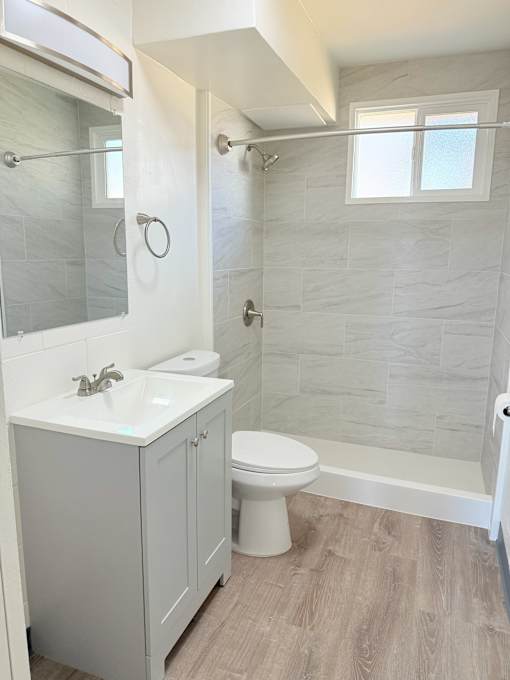 A white toilet sits in a bathroom with a white sink and a walk-in shower.