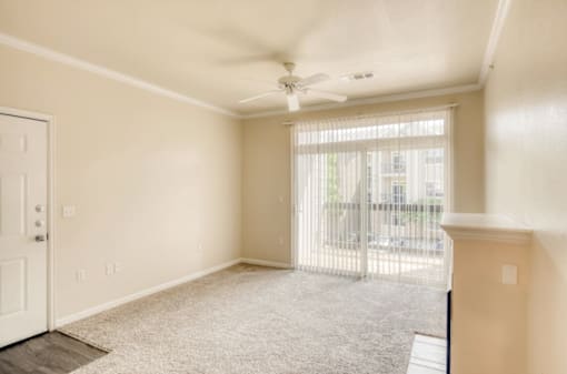 A room with a carpeted floor, a ceiling fan, and a sliding glass door.