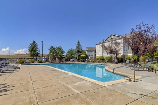 A swimming pool surrounded by a concrete patio and a building in the background.
