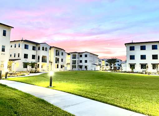 A building complex with a grassy area in front and a pathway leading to the entrance.