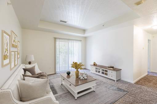 A living room with a white couch, a coffee table, and a window with blinds.