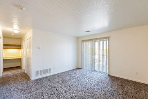 A spacious room with carpeted floor and a sliding glass door.