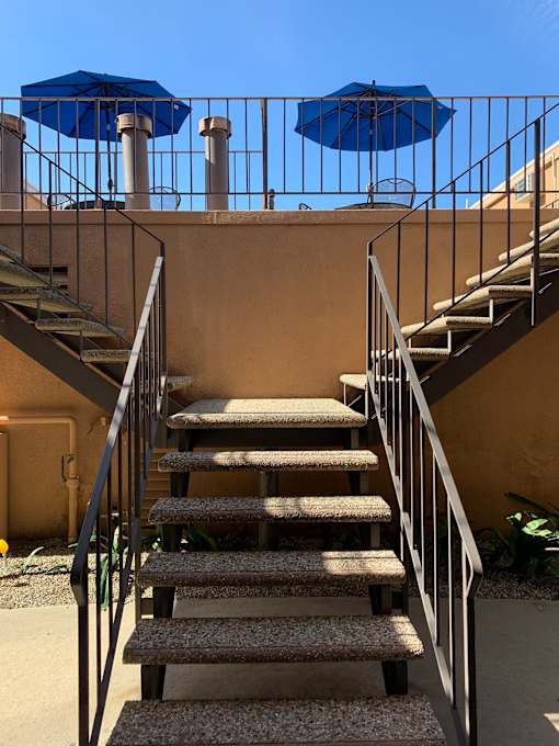 A staircase with a metal railing and a blue umbrella above it.