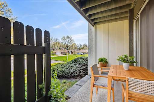 A wooden table and chairs are on a patio with a view of a backyard.
