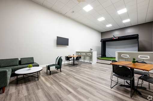 A conference room with a green couch, a white coffee table, and a TV on the wall.