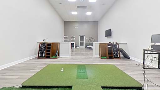 A room with a green mat in the middle and a basketball hoop on the right.