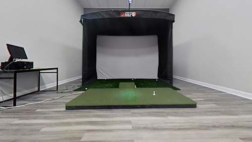 A room with a green artificial turf and a black screen.