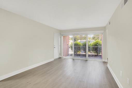 A room with a white door and a window with a view of a fence and trees.