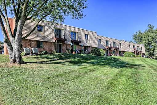 A tree stands in front of a brick building with a lawn in the foreground.