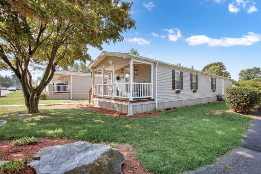 a white mobile home with a porch and a tree