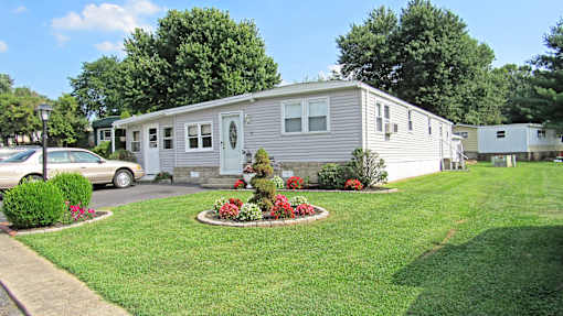 A house with a grey exterior and a white door is surrounded by a green lawn and a flower bed.