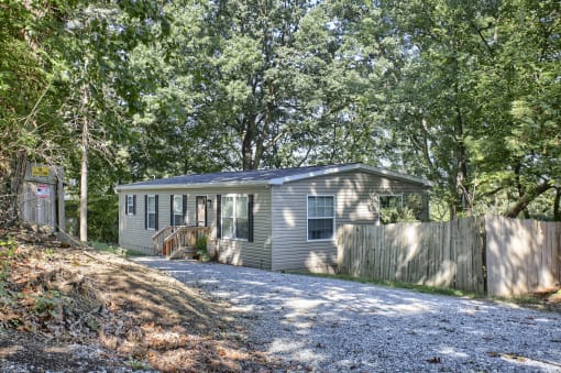 a cottage in the woods with a gravel driveway