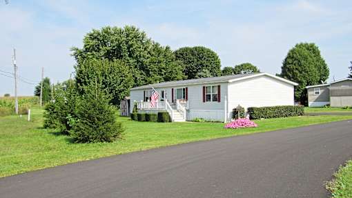 A white house with a flag on the front porch is surrounded by greenery.