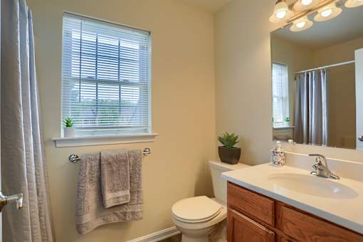 A bathroom with a toilet, sink, and a window with a towel hanging on the wall.