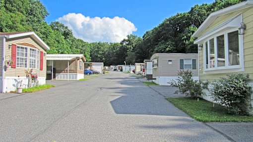 A row of mobile homes with a tree-lined street in the background.