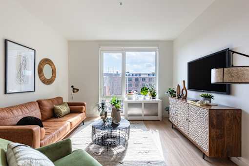 A living room with a brown leather couch, a glass coffee table, and a flat-screen TV mounted on the wall.