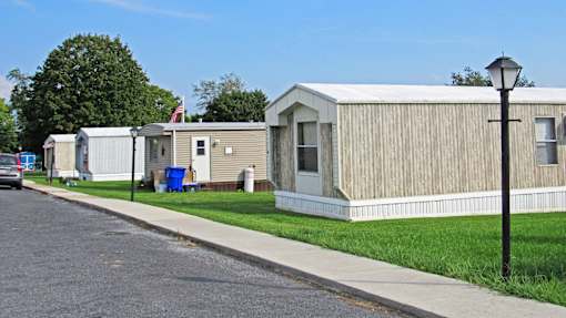 A row of mobile homes with a blue trash can and a flag in the background.