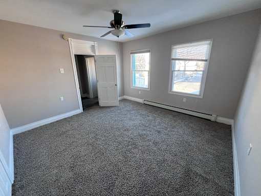 A room with a ceiling fan and two windows.