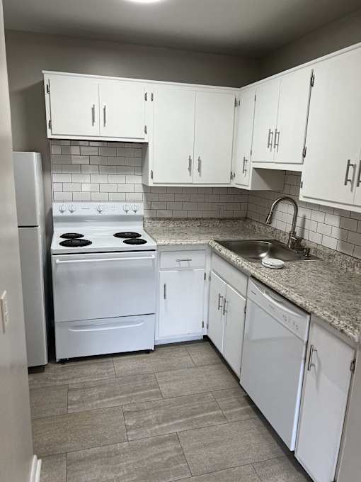 an empty kitchen with white cabinets and appliances and a sink