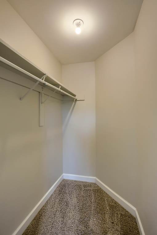 A white wall with a grey carpet and a white ceiling with a light on.