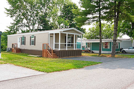 A mobile home with a porch and a car parked in the driveway.