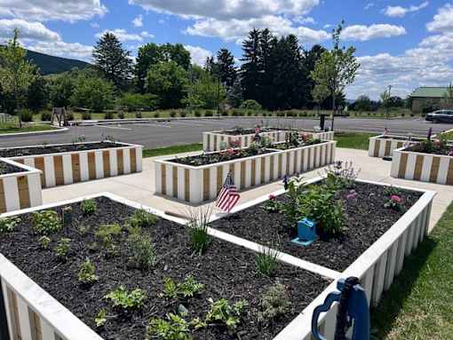 A garden with raised beds and plants in the foreground with a flag in the middle.