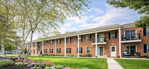 A row of red brick houses with green lawns and trees in front.