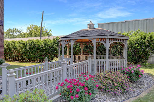 A gazebo surrounded by a white picket fence and pink flowers.