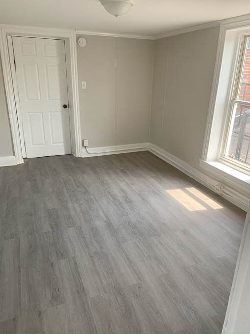 A room with a white door and a window with a grey floor.