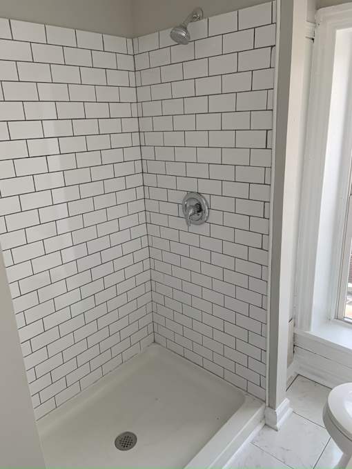A white tiled shower with a drain in the middle.