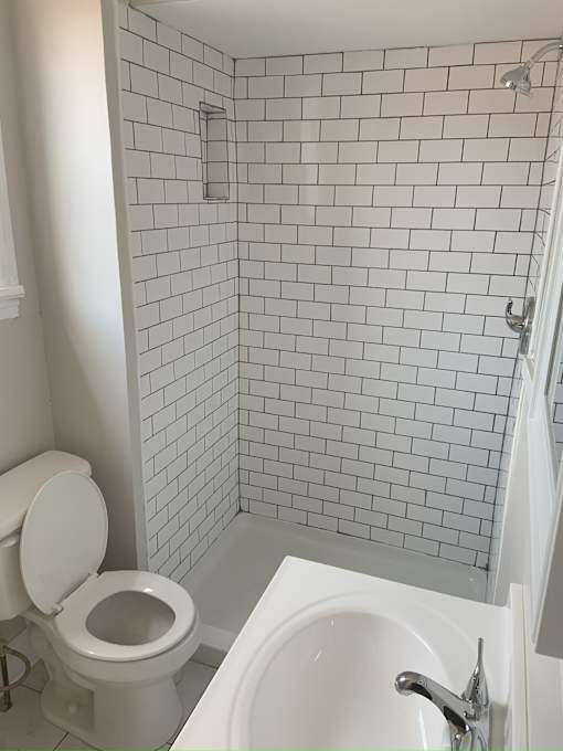 A white toilet sits next to a white sink in a white tiled bathroom.