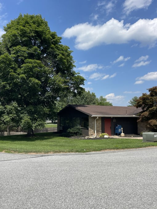 a house on the side of the road with a tree in front of it