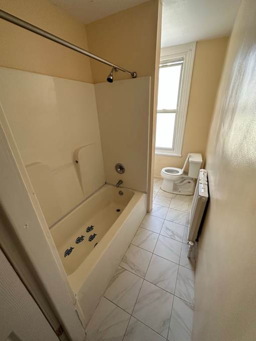 A bathroom with a toilet, tub, and window.