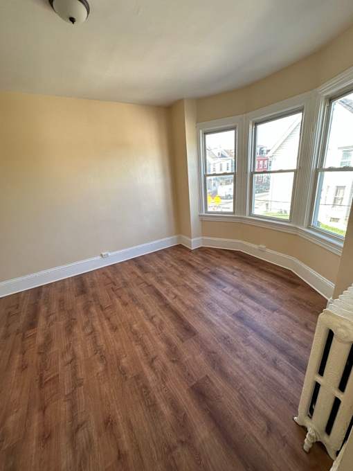 A room with wooden floors and a window overlooking a street.