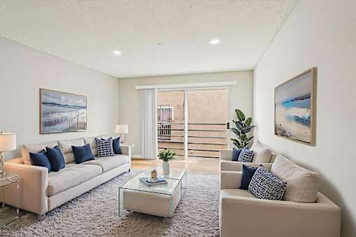A living room with a white couch, a glass coffee table, and a painting on the wall.