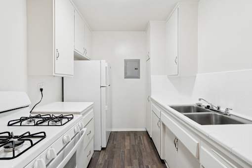 A white kitchen with a stove, sink, and refrigerator.