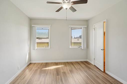 A room with a ceiling fan and two windows.