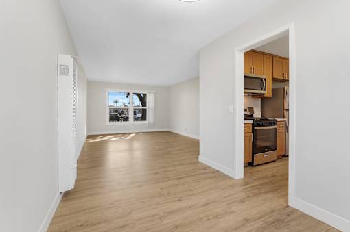 A spacious living room with wooden floors and a kitchen area in the background.
