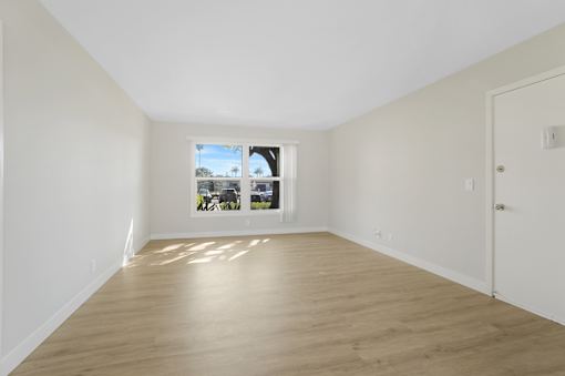 A room with wooden flooring and a window showing a view of trees and a building.